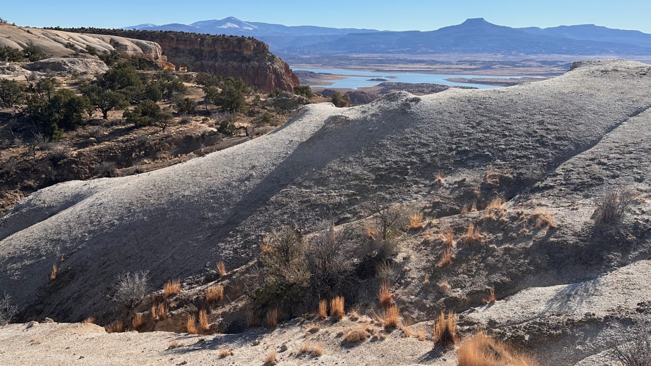 Pale eroded hills above a reservoir, with a flat-topped mesa on the horizon, northern New Mexico.