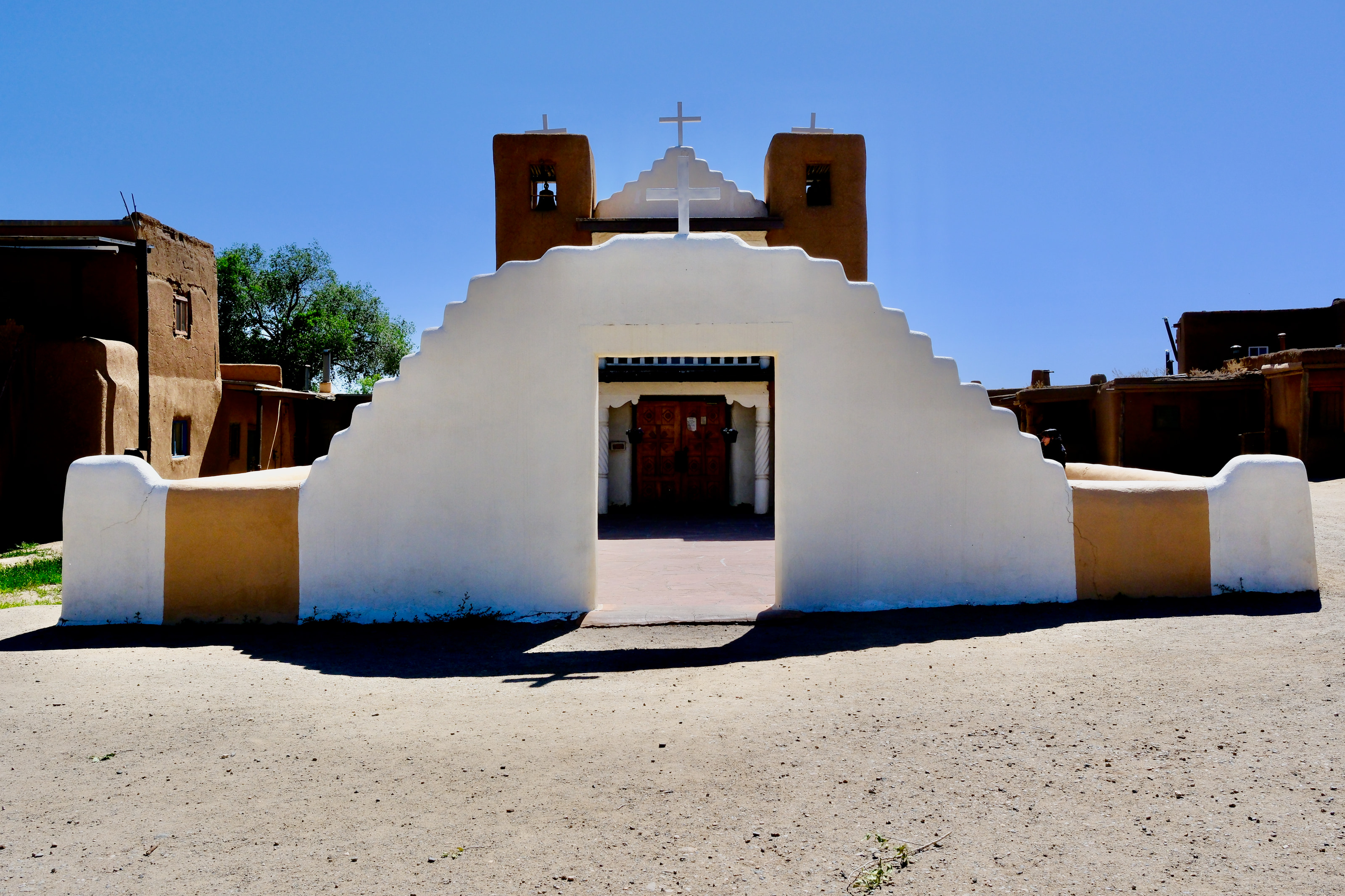A historic adobe mission with community members gathered outside.